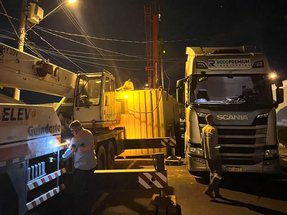 Guindauto munck da Eleva iluminado trabalhando à noite ao lado de um caminhão